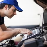 Skilled mechanic using a laptop computer to check a car engine